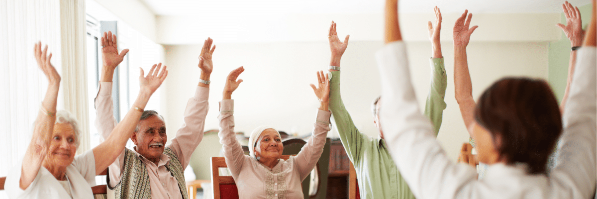 Elderly people sitting on Chairs throwing their hands in the air.